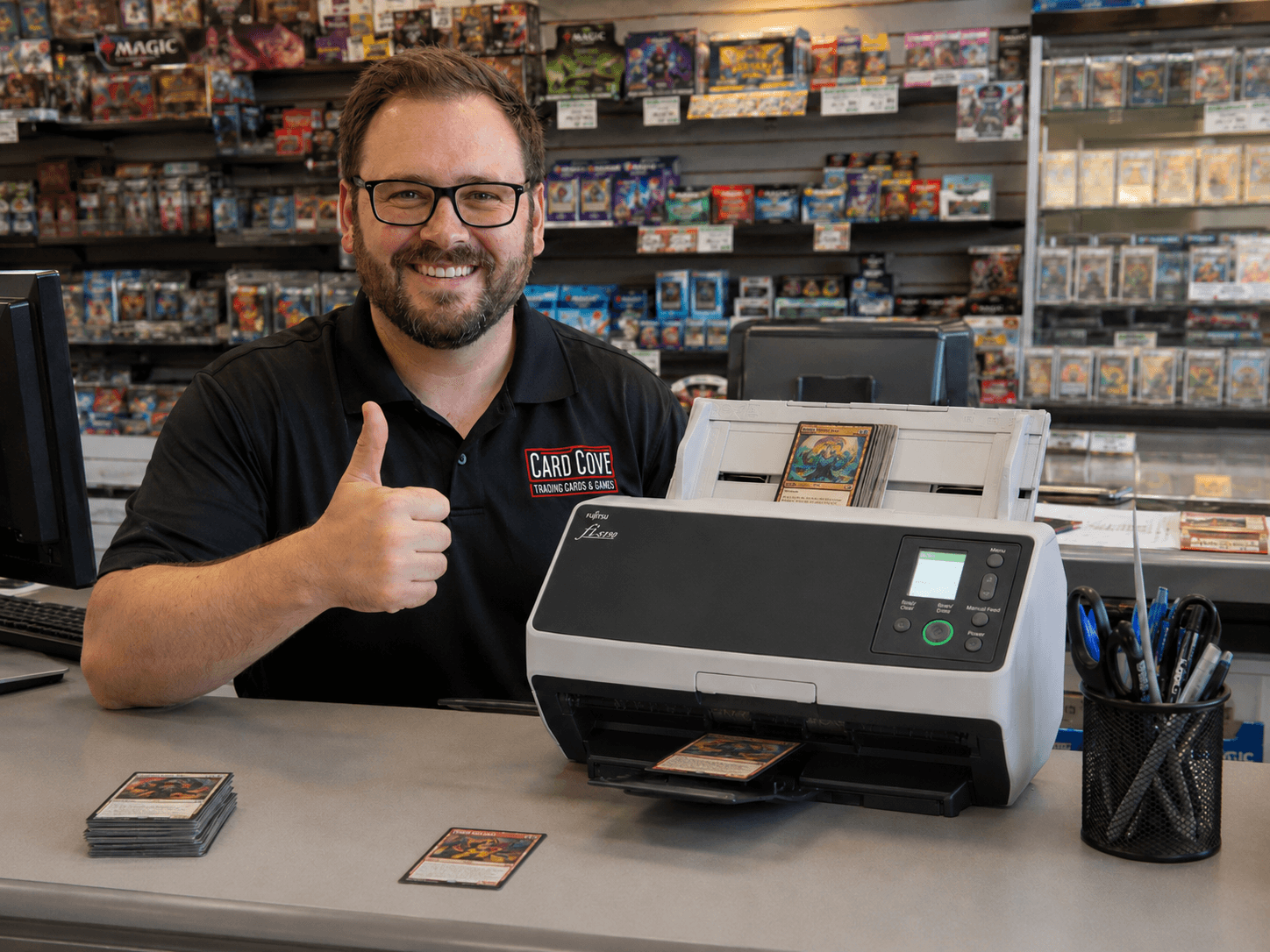 Trading card shop owner standing with the Ricoh scanner, caught up on inventory